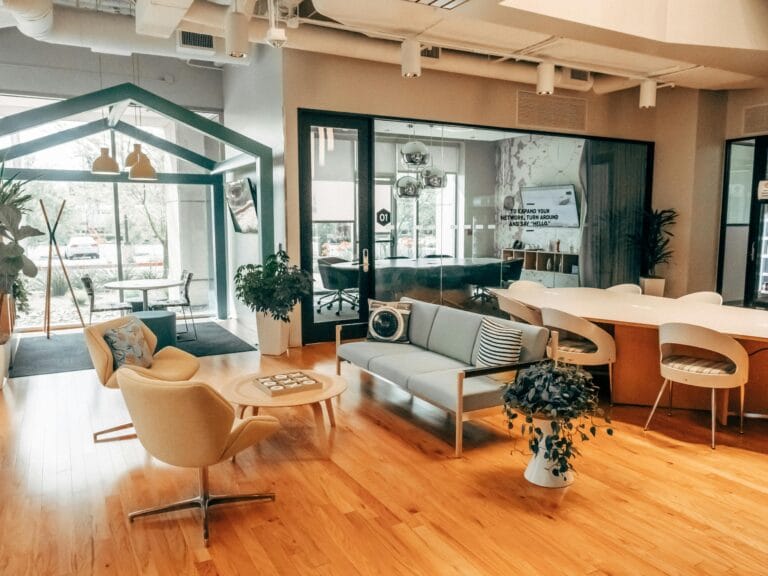 A modern coworking space with stylish seating, wood flooring, and a glass-walled meeting room