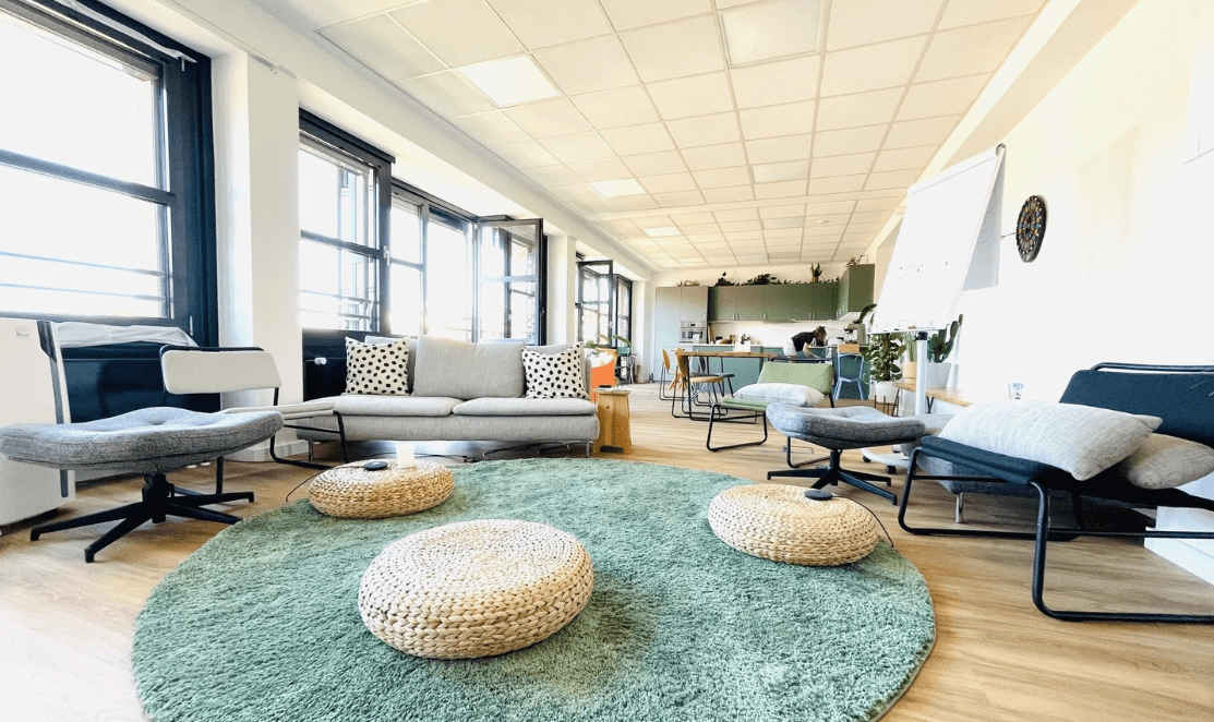 Modern coworking space with cozy seating, green rug, and natural light. Ideal for productive work.