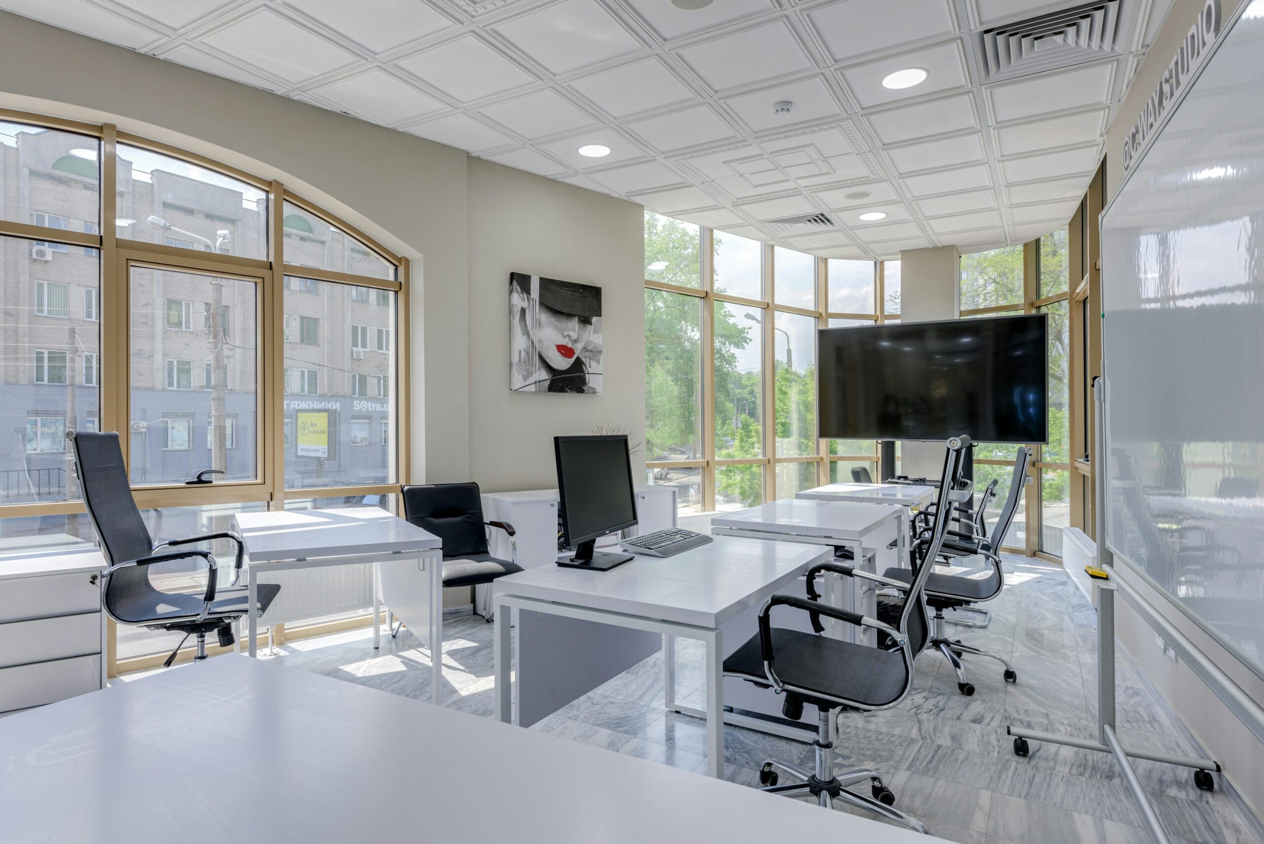 Modern office with bright windows, desks, and a large screen for presentations.