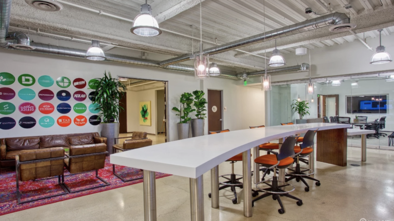 Creative coworking space with high desks, lounge area, exposed ceiling, and modern industrial design.